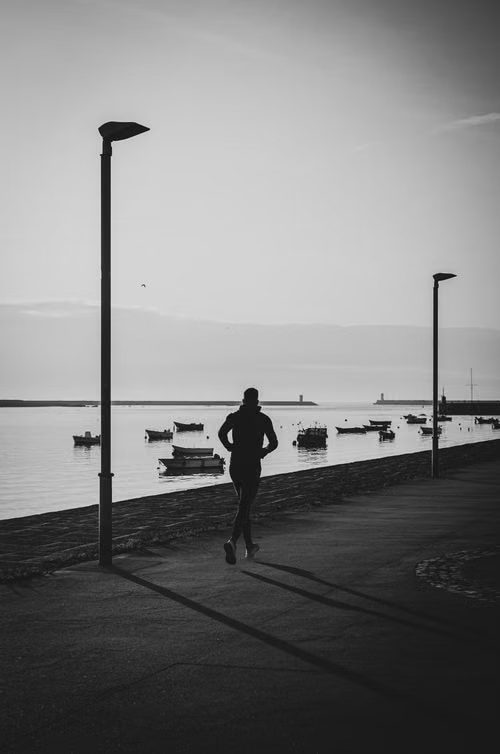 A runner on a waterfront path at dawn, boats moored in the bay