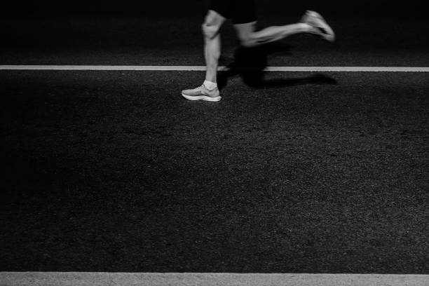 Close-up of a runner's legs mid-stride on dark asphalt between painted lines
